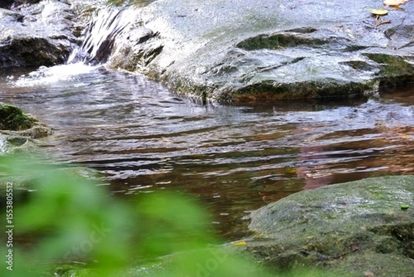 Obraz In selective focus a waterfall with a large stone and blurred green leaves background (Sarika waterfall in Nakornnayok province,Thailand)