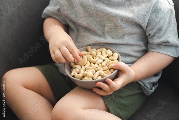 Fototapeta Unrecognizable caucasian toddler sitting on a chair and eating dry cashew nuts. Vegan, healthy eating snack food
