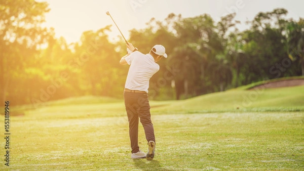 Fototapeta Golfer Finishing a Swing at Sunset on a Golf Course, golfer wearing a white cap and shirt completes a swing on a sunlit golf course.