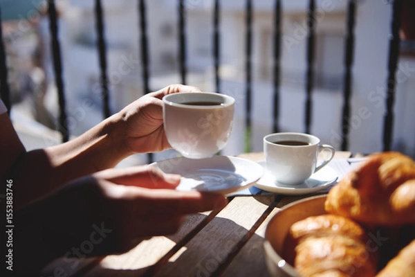 Fototapeta A serene moment enjoying coffee and croissants on a sunlit balcony with blurred urban scenery in the background. Perfect for concepts like relaxation, breakfast, and outdoor leisure.