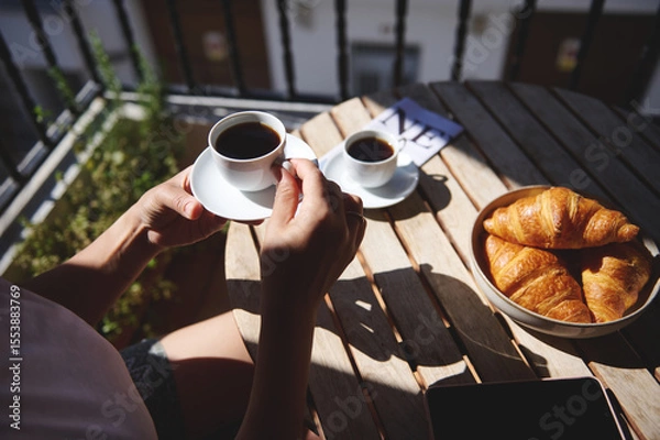 Fototapeta A serene morning setting featuring coffee and croissants on a wooden table. Ideal for enjoying a peaceful start to the day in a natural and fresh environment.