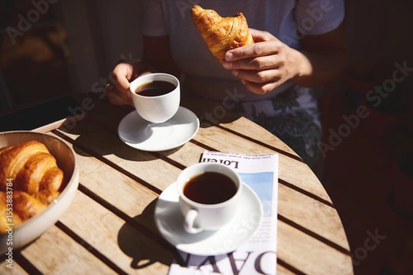 Fototapeta Table setting with coffee, croissants, and a magazine, portraying a peaceful morning routine in natural sunlight.