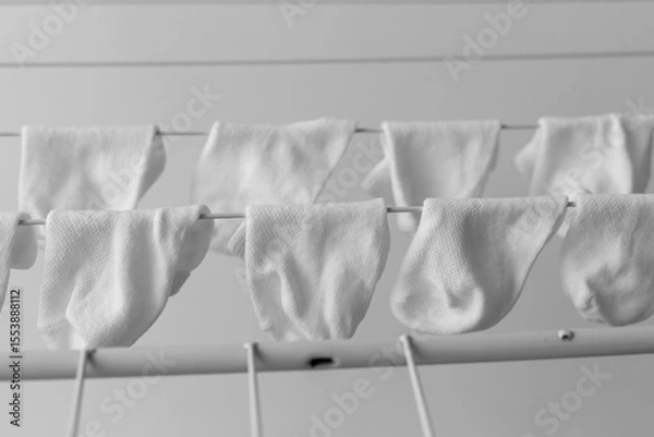 Fototapeta White baby socks neatly hanging on a drying rack indoors, arranged in rows, black and white minimalist photo, concept of parenting and cleanliness