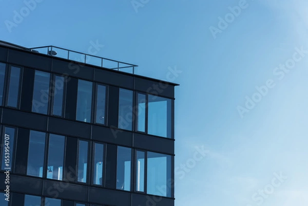 Fototapeta Contemporary office building with large glass windows under clear blue sky, suitable for business or architecture themes. The image highlights modern urban design and corporate environment.