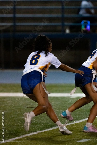 Obraz A female flag football player charges forward with determination during a night game. Capturing speed, focus, and competitive spirit under stadium lights on the turf.