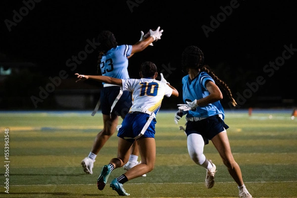 Fototapeta Girls flag football player leaps to catch the ball midair as defenders close in, high-intensity school sports moment under lights, showcasing youth athleticism, teamwork, focus, and determination.