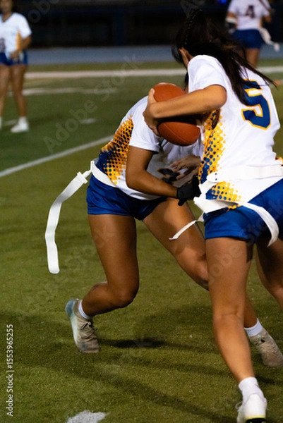 Fototapeta Youth flag football game with blue and white teams playing on grassy field, kids competing in sports under sunny sky, athletic teamwork, childhood activity, outdoor fun, amateur league.