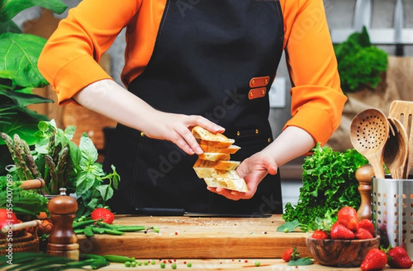 Fototapeta In a bright kitchen, a chef skillfully layers fresh bread while preparing a healthy meal, surrounded by a variety of ingredients.