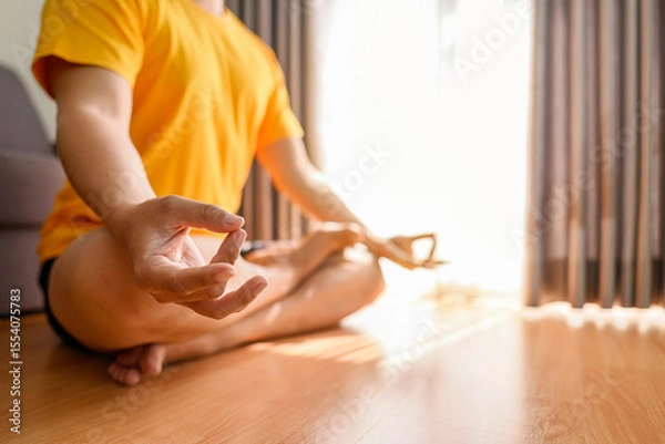 Fototapeta Man meditating in the lotus position on yoga at home for a healthy lifestyle and body care. Meditation and yoga practices concept