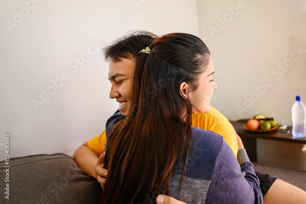 Fototapeta Indonesian southeast asian affectionate couple embracing while sitting on the couch at home