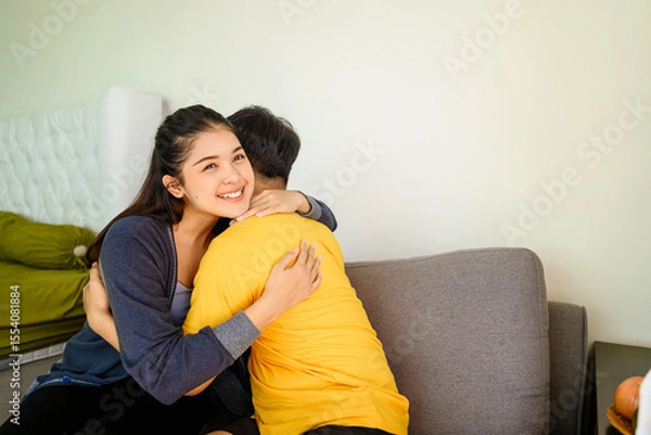 Fototapeta Indonesian southeast asian affectionate couple embracing while sitting on the couch at home