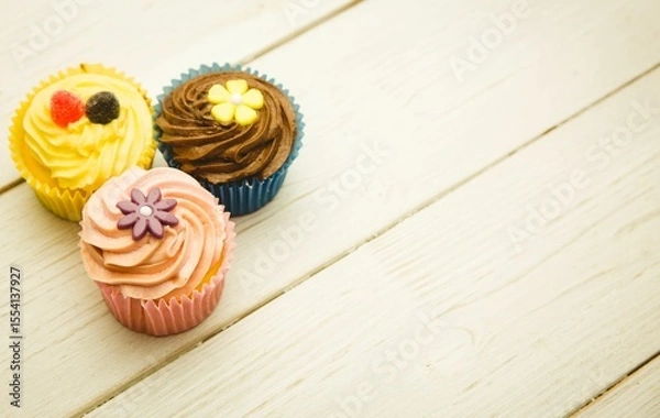 Obraz Three swirl frosting cupcakes with candy toppers are sitting on wooden plank in flat design