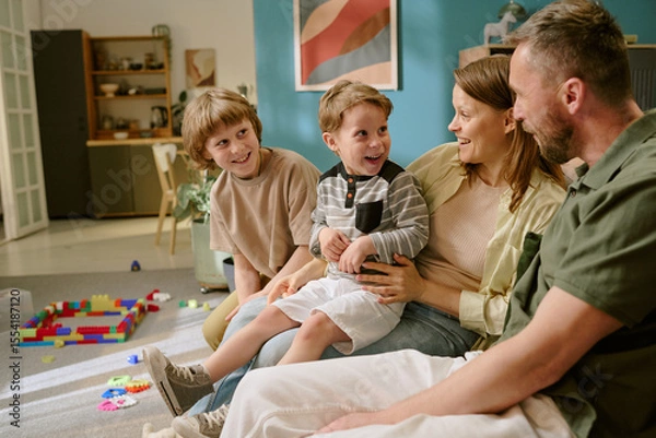 Obraz Caucasian middle aged woman and man sitting on sofa interacting with two Caucasian boys, one child and one teenager, smiling and laughing together in home setting with toys visible