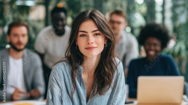 Fototapeta A woman in a pinstripe shirt smiling at the camera with colleagues blurred in the background