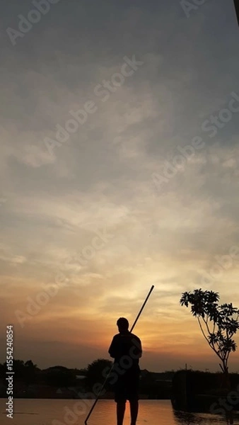 Fototapeta Silhouette of a Person with a Stick at Sunset Sky with Clouds and Tree.