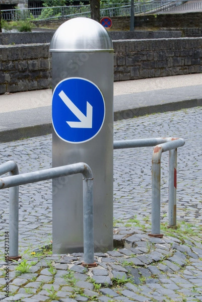 Fototapeta A metal pole in the middle of the roadway, enclosed by a steel frame for safety and bypassing