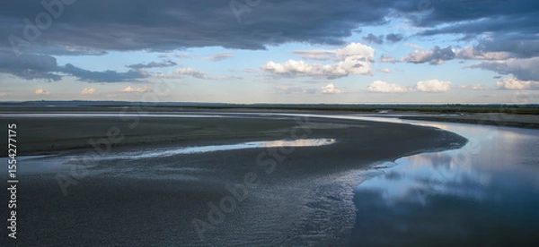Fototapeta Calm waters reflect a dramatic sky at low tide near a tranquil estuary in the late afternoon