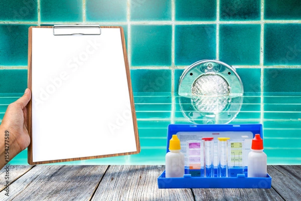 Obraz Water tester test kit and blank report on wooden clipboard over swimming pool light install on the wall, pool light illumination, quality water tester