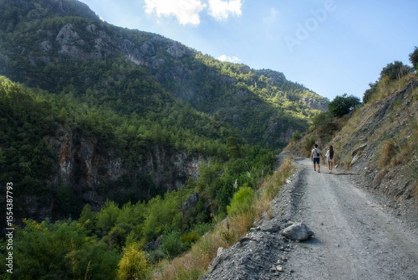 Fototapeta Couple walking on a mountain road surrounded by scenic landscape
