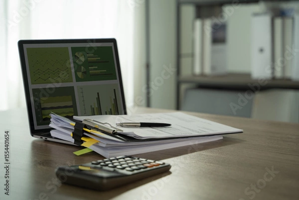 Obraz Report file Eco friendly tidy office workspace with documents, pen, calculator, and laptop displaying charts and graphs, suggesting financial