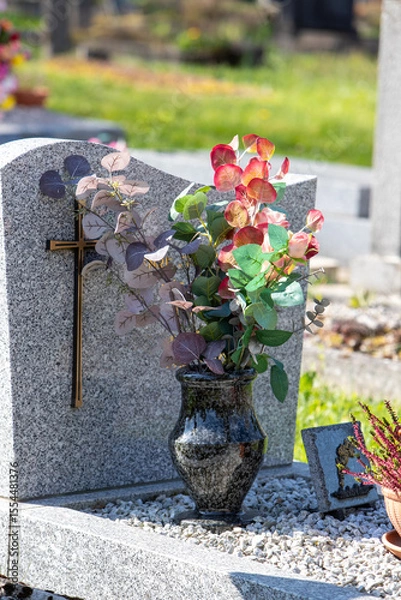 Fototapeta Le fleurissement d’une tombe avec un bouquet de fleurs rouge. Cela permet de rendre hommage au défunt et de témoigner son attachement et le respect envers cet être cher.