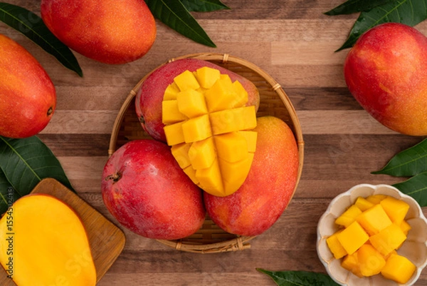 Fototapeta Fresh ripe mango with cubes on wooden table background.