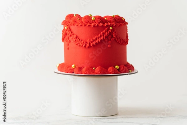 Fototapeta Delicate lambeth style birthday cake with red cream cheese frosting decorated with cream tracery and golden sprinkles. White background