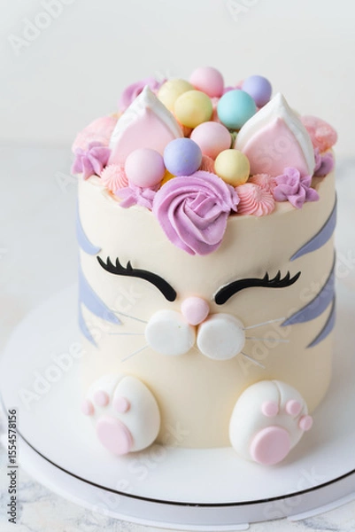 Fototapeta Cute birthday cake in the shape of cat with mastic ears and paws decorated with pink cream fur on the white background. Adorable cake for a little girl who likes cats