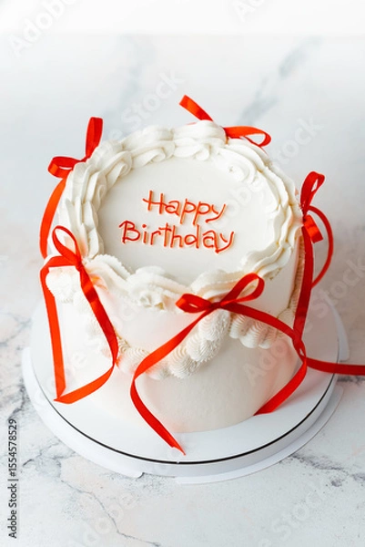 Fototapeta Delicate lambeth style birthday cake with white cream cheese frosting decorated with cream tracery and red happy birthday text on top. White background