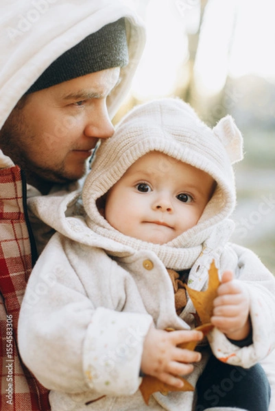 Obraz Happy father hugging and kissing cute baby son in soft evening light in autumn woods. Fatherhood. Stylish man with adorable child in cozy warm sweaters embracing in fall park