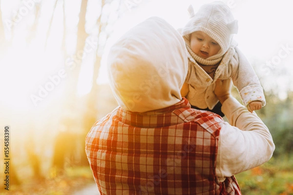 Obraz Happy father holding and playing with cute baby son in soft evening light in autumn woods. Fatherhood. Stylish man with adorable child in cozy warm sweaters having fun in fall park