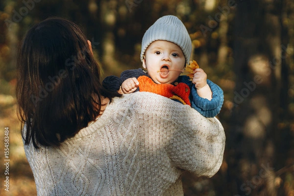 Obraz Happy mother hugging cute baby son in autumn woods. Motherhood. Stylish woman with adorable child in cozy warm sweaters embracing and relaxing in fall park