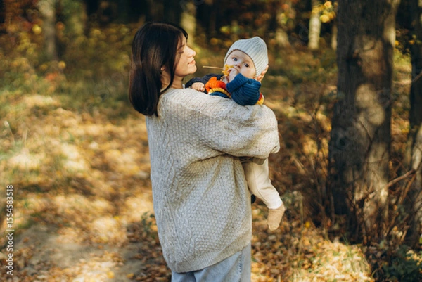 Obraz Happy mother hugging cute baby son in autumn woods. Motherhood. Stylish woman with adorable child in cozy warm sweaters embracing and relaxing in fall park
