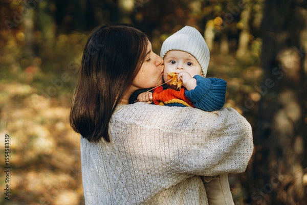 Obraz Happy mother hugging and kissing cute baby son in autumn woods. Motherhood. Stylish woman with adorable child in cozy warm sweaters relaxing in fall park