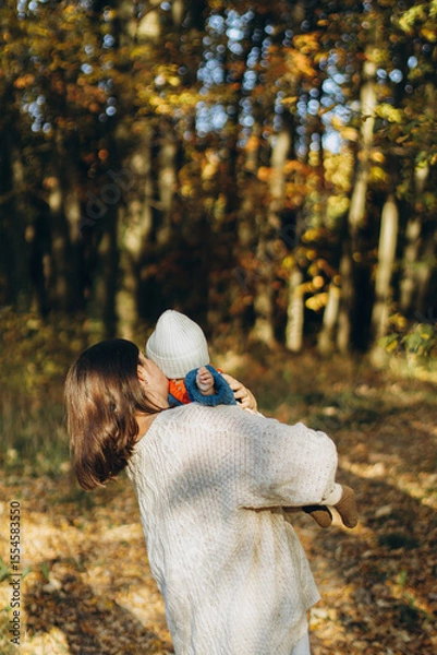 Obraz Happy mother hugging cute baby son in autumn woods. Motherhood. Stylish woman with adorable child in cozy warm sweaters embracing and relaxing in fall park