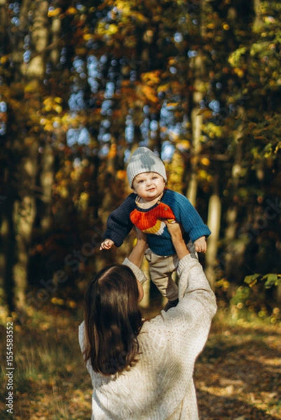 Obraz Happy mother playing with cute baby son in autumn woods. Motherhood. Stylish woman with adorable child in cozy warm sweaters having fun and relaxing in fall park