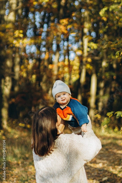 Obraz Happy mother playing with cute baby son in autumn woods. Motherhood. Stylish woman with adorable child in cozy warm sweaters having fun and relaxing in fall park
