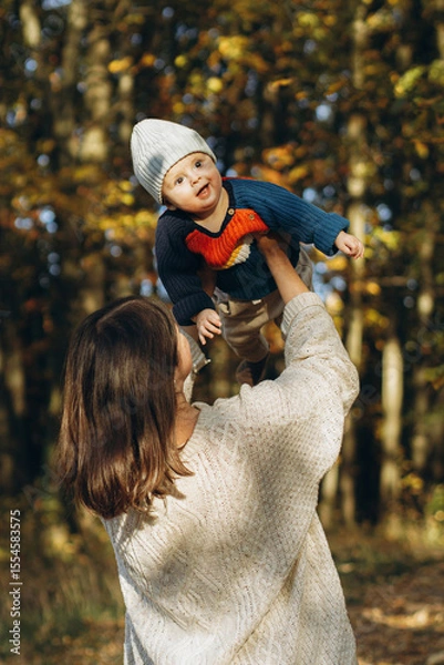 Obraz Happy mother playing with cute baby son in autumn woods. Motherhood. Stylish woman with adorable child in cozy warm sweaters having fun and relaxing in fall park