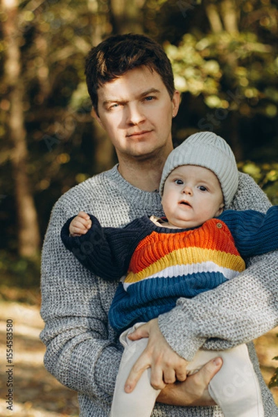 Obraz Happy father hugging cute baby son in autumn woods. Fatherhood. Stylish man with adorable child in cozy warm sweaters having fun and relaxing in fall park
