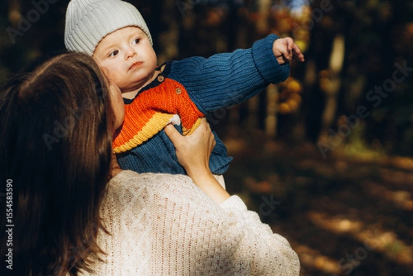 Obraz Happy mother hugging and kissing cute baby son in autumn woods. Motherhood. Stylish woman with adorable child in cozy warm sweaters embracing and relaxing in fall park