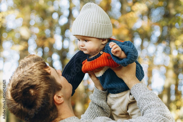 Obraz Happy father playing with cute baby son in autumn woods. Fatherhood. Stylish man with adorable child in cozy warm sweaters having fun and relaxing in fall park
