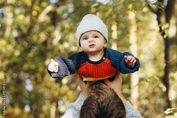 Obraz Cute baby son with funny emotions in father hands close up in autumn woods. Fatherhood. Stylish man with adorable child in cozy warm sweaters having fun and relaxing in fall park