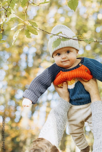 Obraz Cute baby son with funny emotions in father hands close up in autumn woods. Fatherhood. Stylish man with adorable child in cozy warm sweaters having fun and relaxing in fall park