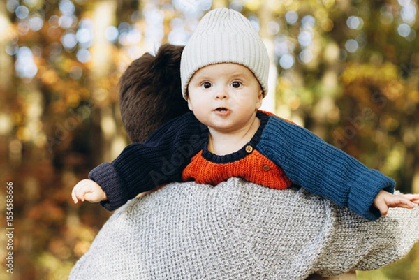 Obraz Cute happy baby son with funny emotions close up in father hands  in autumn woods. Fatherhood. Stylish man with adorable child in cozy warm sweaters relaxing in fall park