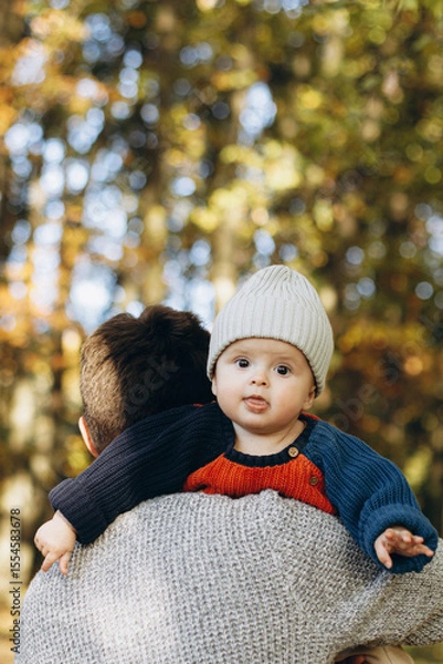 Obraz Cute happy baby son with funny emotions close up in father hands  in autumn woods. Fatherhood. Stylish man with adorable child in cozy warm sweaters relaxing in fall park