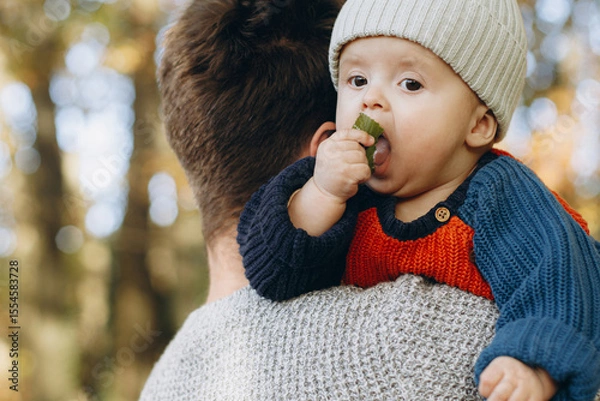 Obraz Cute baby son with funny emotions holding leaves close up in father hands  in autumn woods. Fatherhood. Stylish man with adorable child in cozy warm sweaters relaxing in fall park