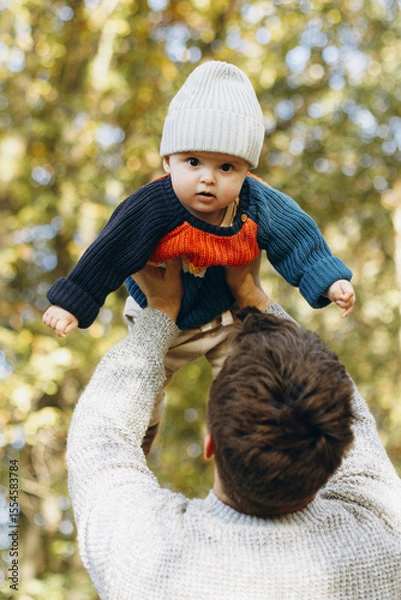 Obraz Happy father playing with cute baby son in autumn woods. Fatherhood. Stylish man with adorable child in cozy warm sweaters having fun and relaxing in fall park
