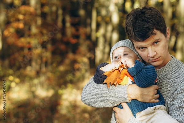 Obraz Happy father hugging cute baby son in autumn woods. Fatherhood. Stylish man with adorable child in cozy warm sweaters embracing and relaxing in fall park