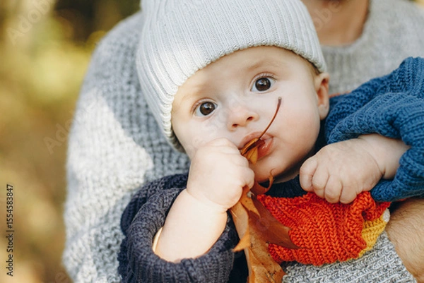 Obraz Cute baby son with funny emotions holding leaves close up in father hands  in autumn woods. Fatherhood. Stylish man with adorable child in cozy warm sweaters relaxing in fall park