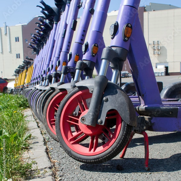 Obraz A lineup of colorful electric scooters parked on a city sidewalk awaiting rental on a bright summer day. Photo